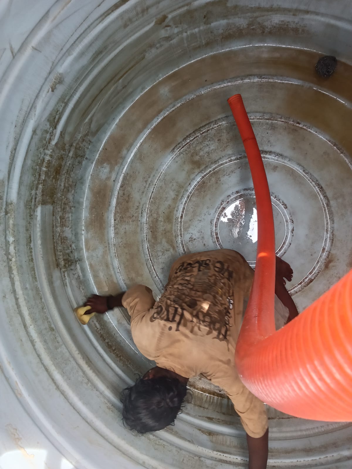 Hemavathi technician scrubbing the inside wall of a residential water sump tank with a suction hose in place