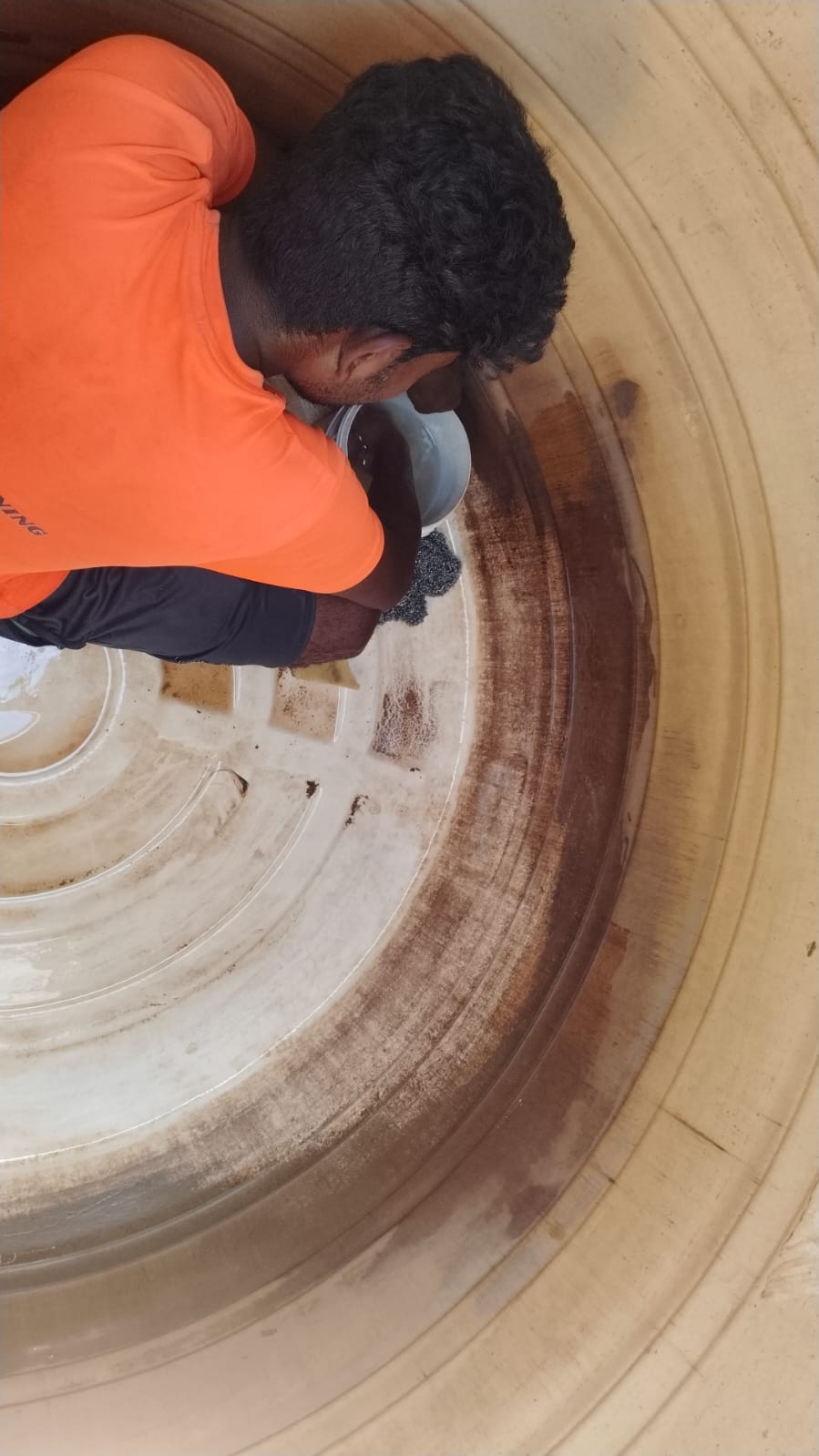 Technician removing sludge and stains from the base of an overhead water tank with a scrub pad